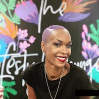 a woman in a black shirt is smiling in front of a colorful wall